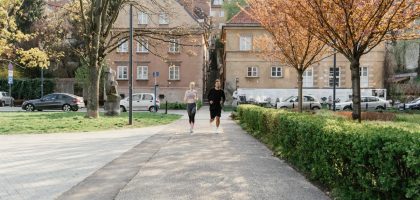 A couple jogging together in an urban park surrounded by greenery and houses.